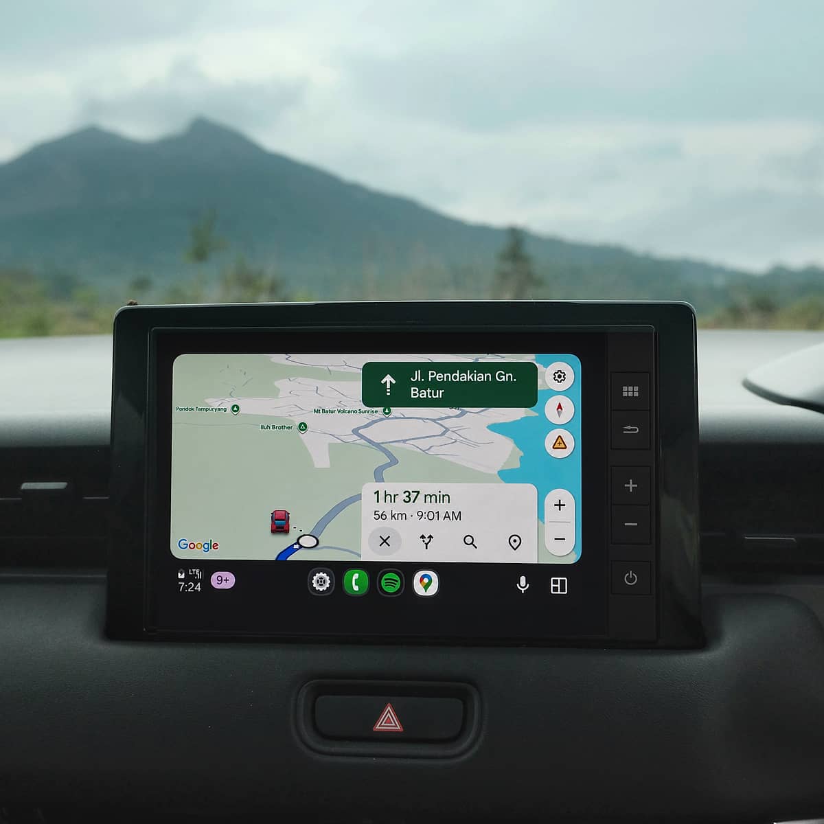 Close-up of a car's infotainment system with a navigation app guiding through Bali's landscape.