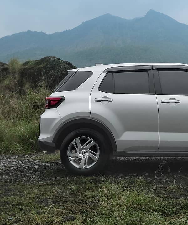 Silver Toyota Raize with black trim parked in a grassy, mountainous landscape.