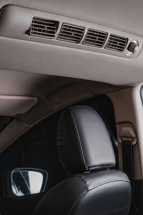 Interior view of a car's rear air conditioning vents, with black leather headrests visible in the foreground.